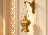 Ornate gold bakhoor burner with Arabic design, hanging chain, and incense smoke