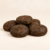 Five dark brown compressed tea cakes with visible earthy texture, arranged in a small pile on a light beige background.
